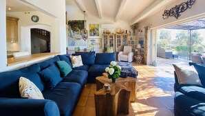 A spacious living room with a large blue sofa, wooden coffee table, and a view of the outdoor patio area. - Charming 5 bedroom, 3 bathroom Villa in gated domain near Valbonne with sea view (Opio)