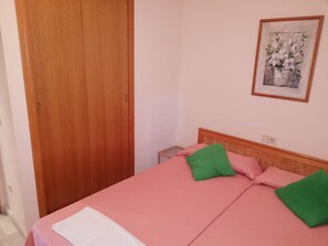 Ein Schlafzimmer mit einem Holzschrank, einem Bett mit rosa Bettwäsche und grünen Kissen sowie einem gerahmten Bild an der Wand.