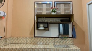 Una cocina con salpicadero de azulejos, un lavabo doble y una pequeña estantería con cristalería y un florero.