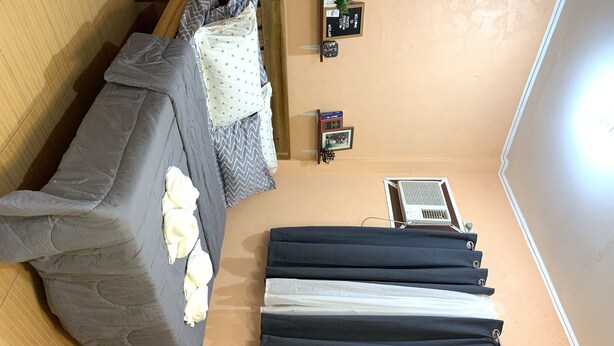 Una habitación con un sofá gris, una mesita con un reloj y un cartel de bienvenida, y una ventana con persianas.