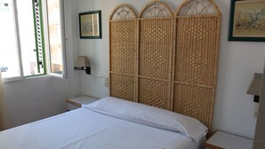 A room with a bed, a nightstand, a lamp, and a window with a view of buildings. - Deltamar 24 Solo Familias! (Xeraco Playa)
