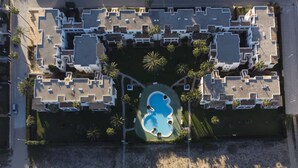 An aerial view of a resort with multiple buildings, a central swimming pool, and surrounding palm trees. - Deltamar 24 Solo Familias! (Xeraco Playa)