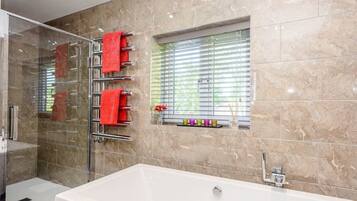 A modern bathroom with a large white bathtub, a glass shower enclosure, and a window with blinds.