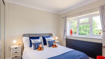 A bedroom with a bed, two nightstands, a window with curtains, and a view of greenery outside.