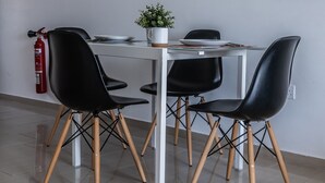 A dining area with a white table, black chairs with wooden legs, a potted plant, and a fire extinguisher on the wall. - Luxurious Unique Apartment (Paralimni)