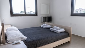 A modern hotel room with a single bed, a bedside table with a remote control, and two windows offering a view of the cityscape. - Luxurious Unique Apartment (Paralimni)