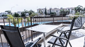 A balcony with a pool, outdoor seating, and a view of residential buildings. - Luxurious Unique Apartment (Paralimni)