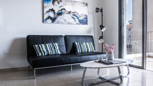 A modern living room with a black leather sofa, striped pillows, a white coffee table, and a large abstract painting on the wall. - Luxurious Unique Apartment (Paralimni)