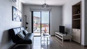 A modern living room with a black leather sofa, a white coffee table, a TV on a stand, and a sliding glass door leading to an outdoor area. - Luxurious Unique Apartment (Paralimni)