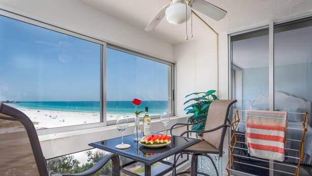 Un balcón con una mesa, una silla, una planta y vistas a la playa.