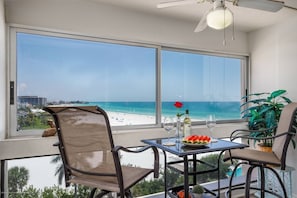 A balcony with a table, chairs, a potted plant, and a view of the beach and ocean. - 7th-Floor Oceanfront Condo on Private Beach (Siesta Key)