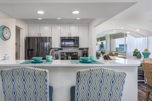 A modern kitchen with white cabinets, stainless steel appliances, and a central island with blue-patterned chairs.