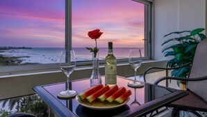 Un balcón con una mesa dispuesta para dos personas, que incluye una botella de vino, una rosa y rebanadas de sandía.