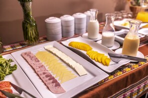 Ein Buffet mit verschiedenen Speisen, darunter Aufschnitt, Käse und Früchte, sowie Soßen und Milchflaschen.
