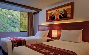 Ein Hotelzimmer mit zwei Betten, einem großen Fenster und Blick auf Grünflächen, einem Bild an der Wand und einer gemusterten Decke auf den Betten.