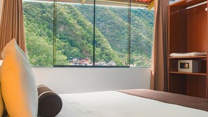 Une chambre d’hôtel avec un lit, une fenêtre donnant sur une montagne boisée et une étagère en bois sur laquelle se trouve un four à micro-ondes.