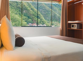 Une chambre d’hôtel avec un lit, une fenêtre donnant sur une montagne boisée et une étagère en bois sur laquelle se trouve un four à micro-ondes.