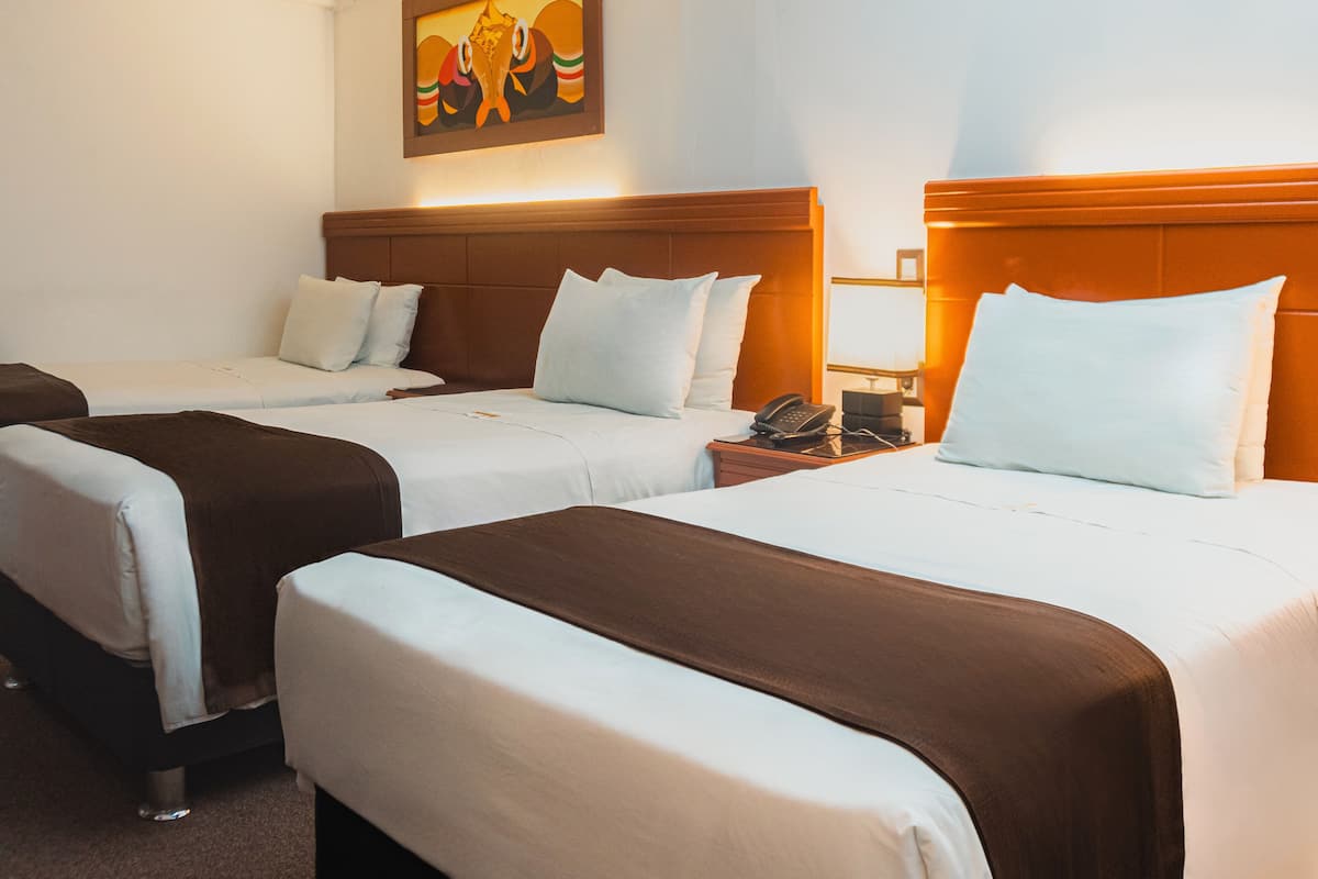 A hotel room with two beds, each with white linens and brown headboards. There is a painting on the wall above the beds and a telephone on the nightstand.