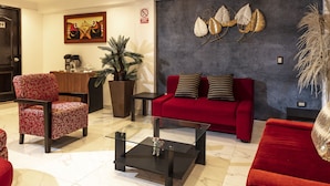 Un salon moderne avec un canapé rouge, des fauteuils à motifs, une table basse et des œuvres d’art décoratives accrochées au mur.