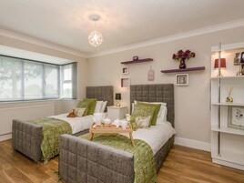 Un dormitorio con dos camas, una mesita de noche con lámpara, una estantería con objetos decorativos y una ventana con persianas.