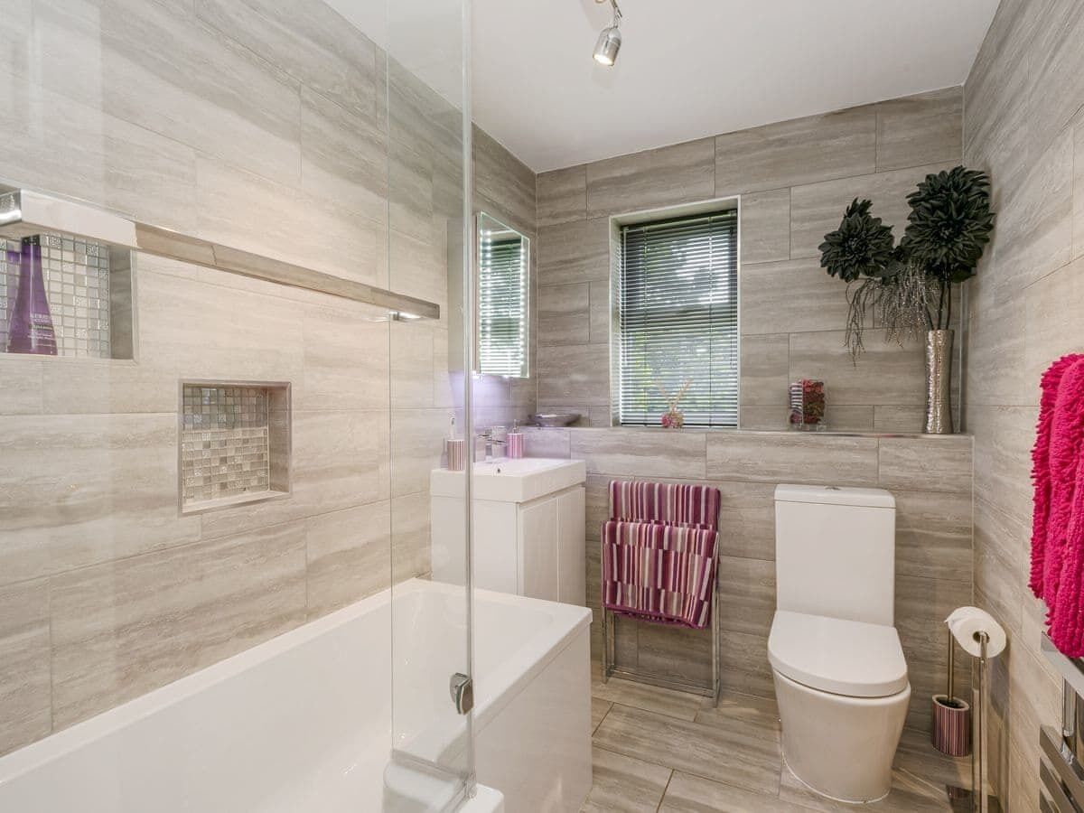 A modern bathroom with a glass-enclosed shower, a white bathtub, a toilet, and a vanity with a mirror.