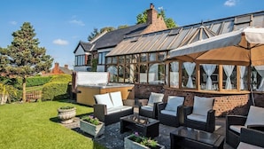 Un espace patio aménagé avec du mobilier d’extérieur, un jacuzzi et une pièce fermée par des parois vitrées.