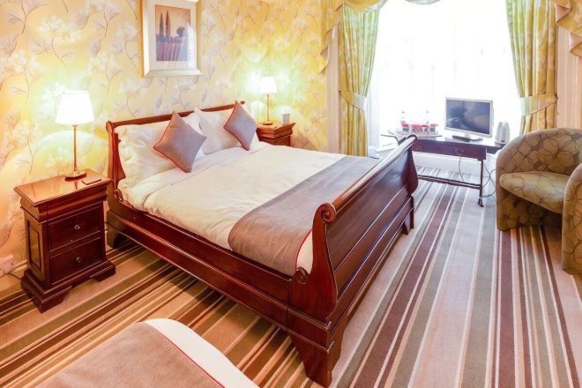 Quarto de hotel com uma cama grande, mesas de cabeceira, escrivaninha, cadeira e televisão.