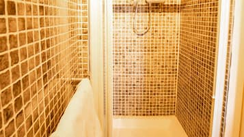 A small, tiled shower room with a white showerhead and a handheld shower attachment.