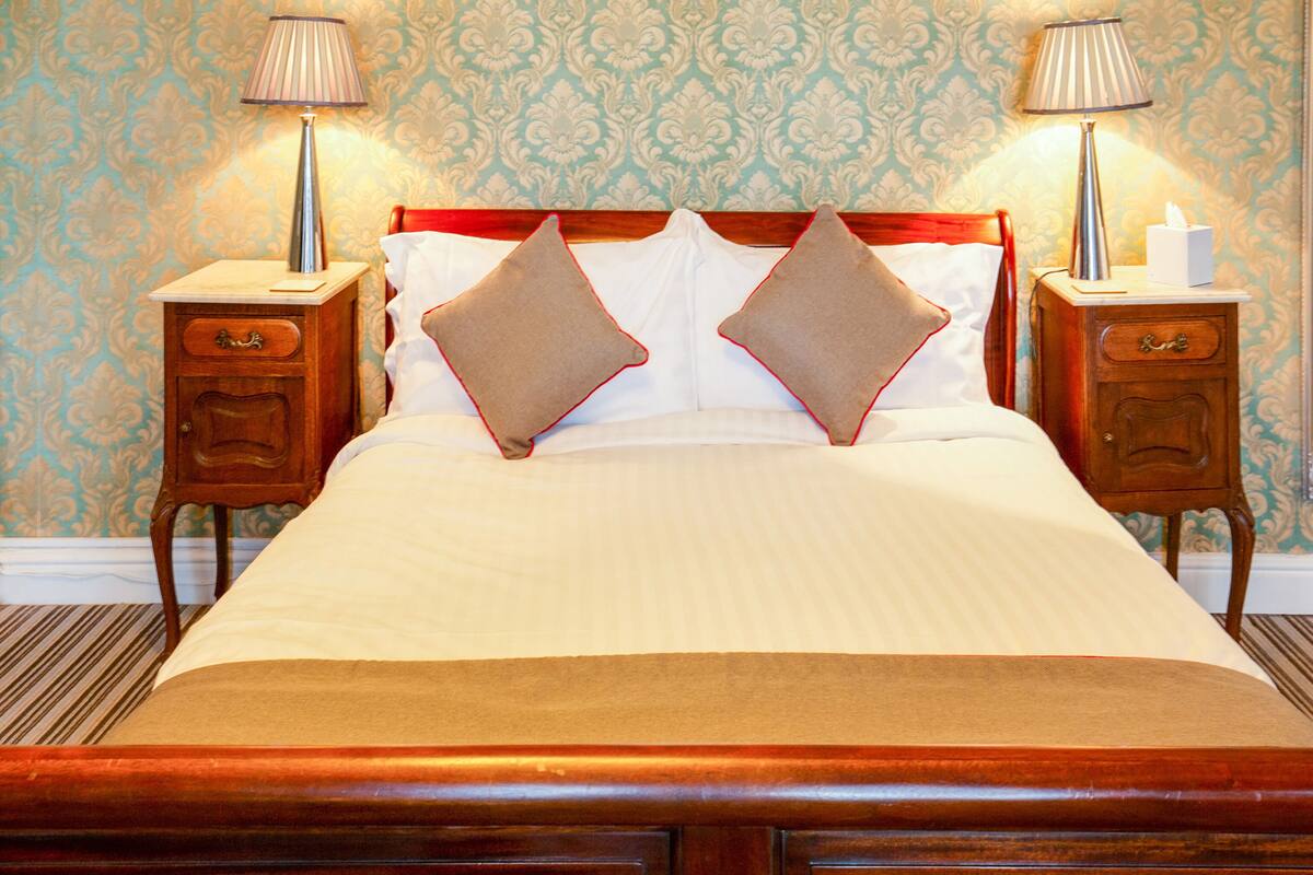 A neatly made bed with two pillows, a wooden headboard, and two bedside tables with lamps.