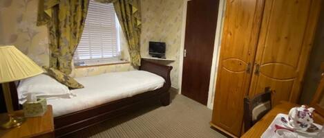 A hotel room with a bed, a desk with a lamp, a television, a wardrobe, and a dining table with a tray.