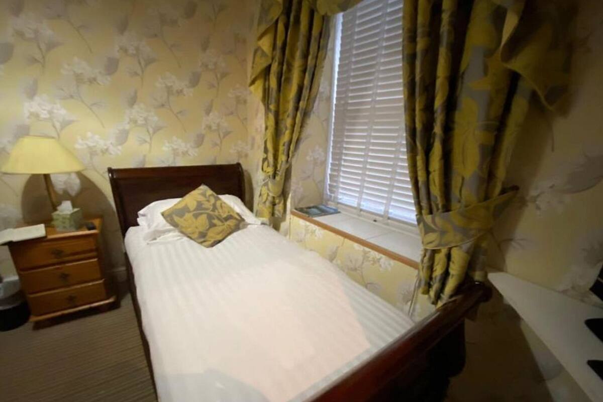 A bedroom with a bed, a nightstand with a lamp, and a window with curtains.