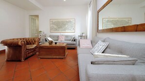 Ein Wohnzimmer mit einem braunen Ledersofa, einem grauen Sofa und einem Holztisch. An den Wänden befinden sich zwei gerahmte Kunstwerke und ein großer Spiegel über dem grauen Sofa.