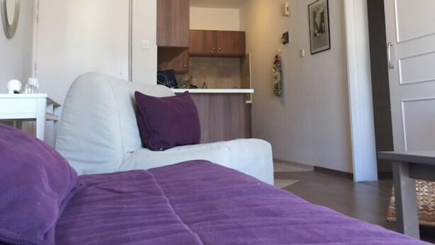 A bedroom with a bed, a desk, and a kitchenette in the background. - Unique 2 bedroom modern apartment (Ayia Napa)