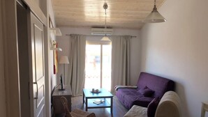 A room with a purple sofa, a small table, a wicker chair, and a ceiling fan. - Unique 2 bedroom modern apartment (Ayia Napa)