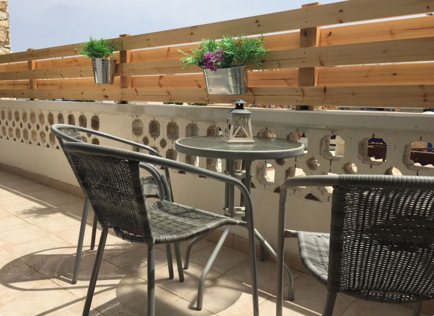 A terrace with wicker chairs and a small round table, a wooden fence, and potted plants.