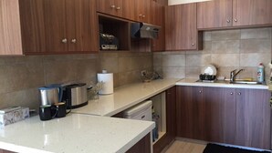 A kitchen with wooden cabinets, a countertop, a sink, and various appliances. - Unique 2 bedroom modern apartment (Ayia Napa)
