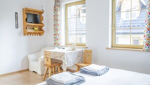 A bedroom with a bed, a desk, and a chair. There is a window with curtains and a view of buildings outside. - Willa Ślimakówka (Zakopane)