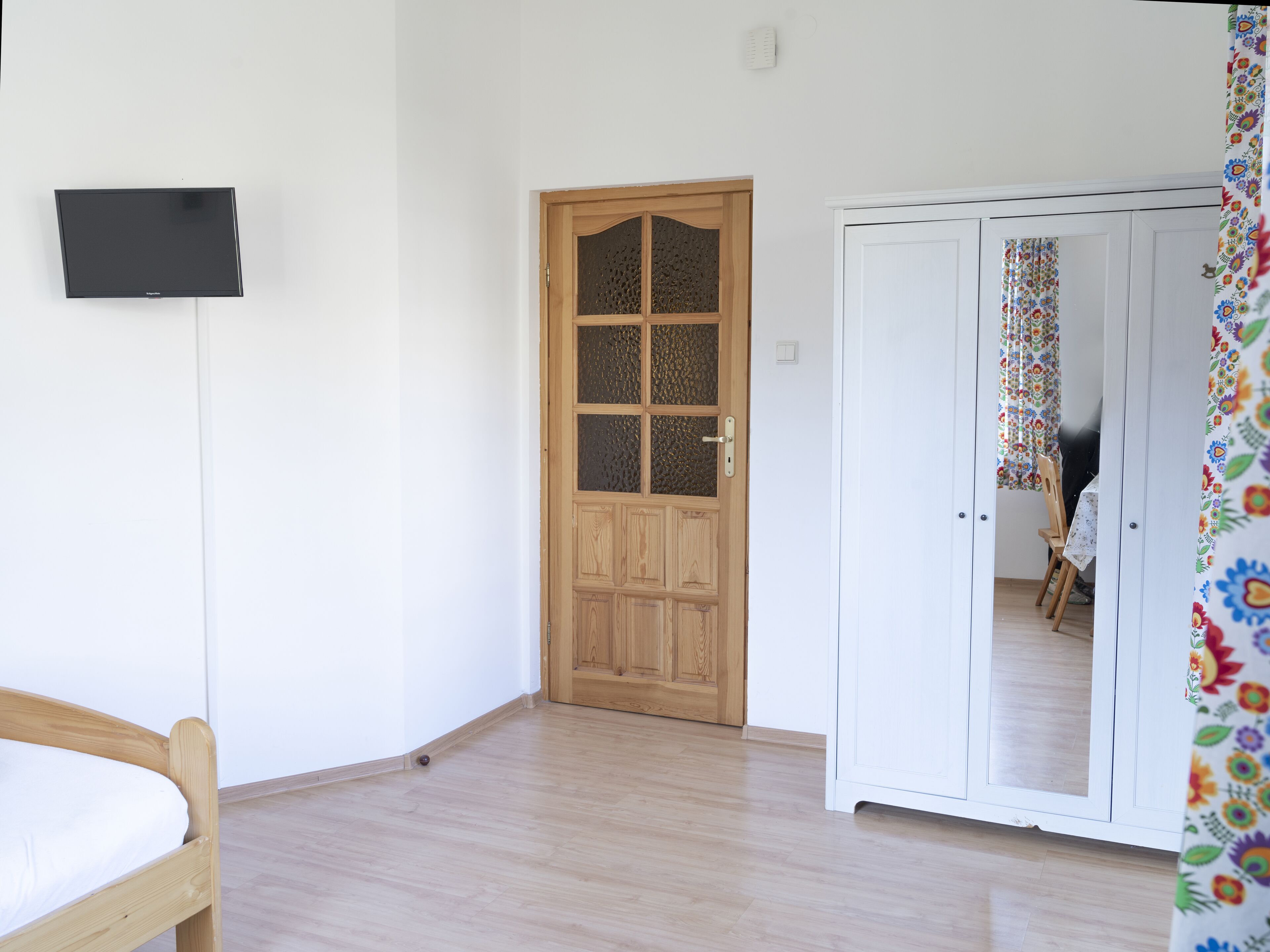 Una stanza con una porta in legno, un letto, un armadio e un televisore appeso al muro.