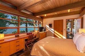 A bedroom with a large bed, wooden desk, and a view of the ocean.