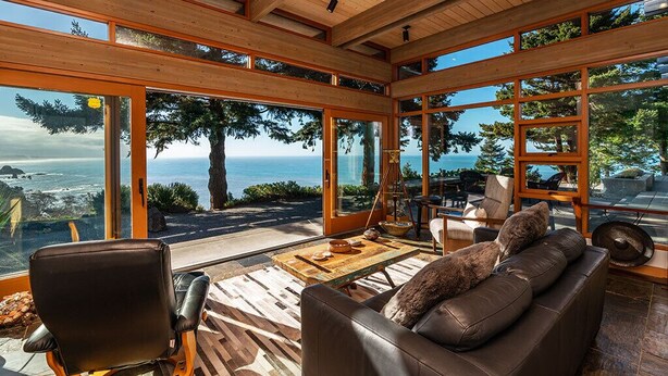 A spacious room with large windows offering ocean views, a leather sofa, and a wooden table with chairs. - Sanctuary House - Architectural Gem w/ Ocean Views! (Trinidad)