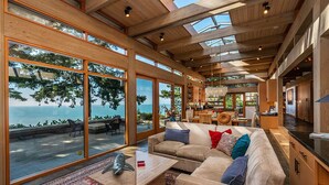 A spacious living area with large windows overlooking a scenic ocean view, wooden ceiling beams, and a cozy seating arrangement. - Sanctuary House - Architectural Gem w/ Ocean Views! (Trinidad)