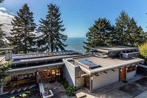 A modern house with a flat roof, solar panels, and a view of the ocean.