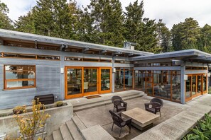 A modern house with a patio area featuring outdoor seating and a view of the surrounding forest. - Sanctuary House - Architectural Gem w/ Ocean Views! (Trinidad)