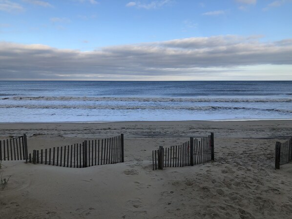A beach with a wooden fence in the foreground and the ocean in the background.