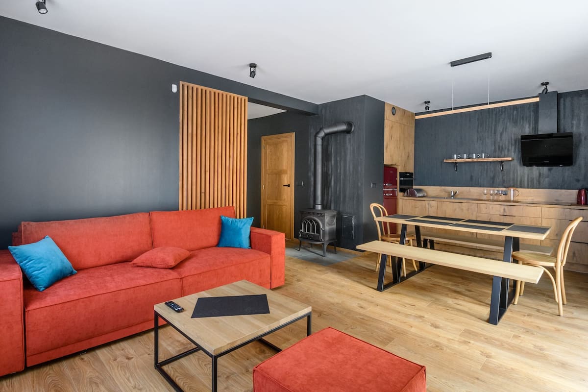 Een moderne woonkamer met een rode bank, een houten eettafel en een klein bijzettafeltje.