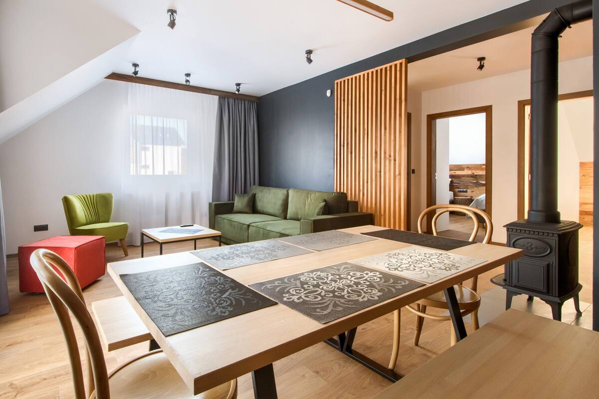 Een moderne woonkamer met een houten eettafel, een groene bank en een rode fauteuil.