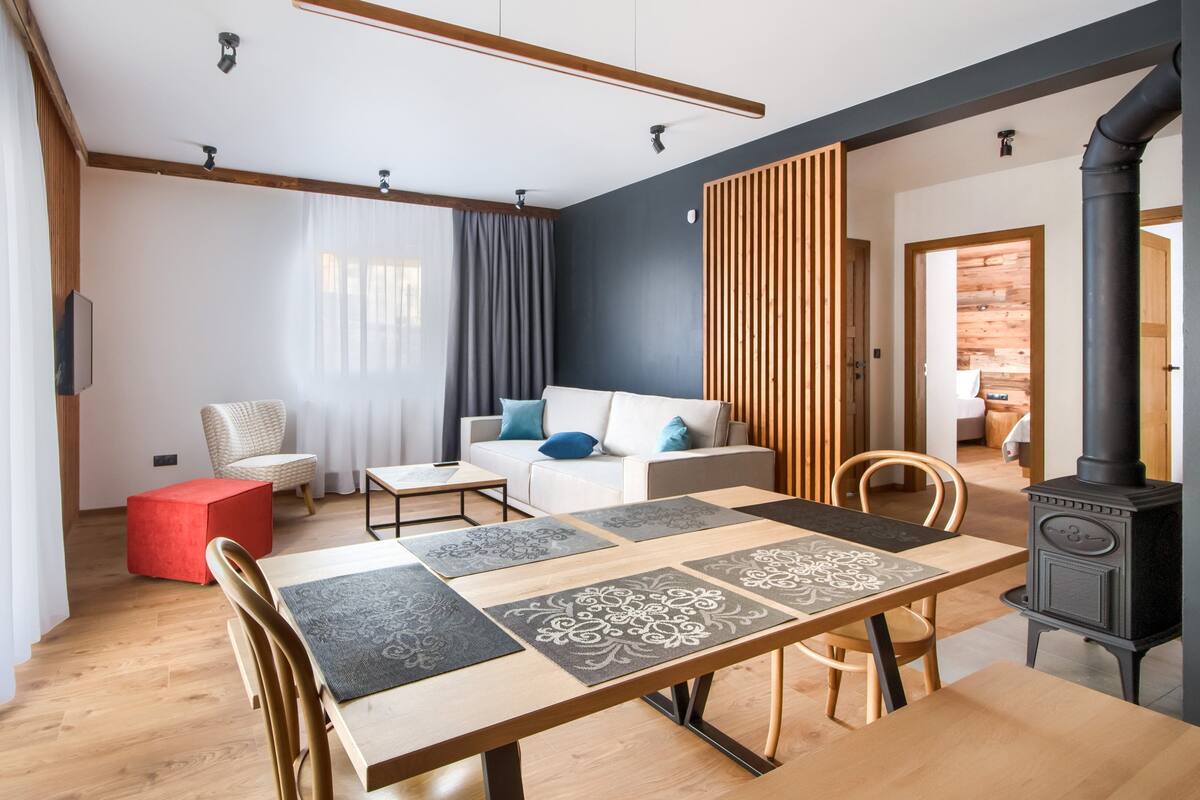 Een moderne woonkamer met een houten eettafel, een bank en een rode poef.