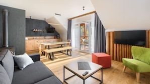 Un salon moderne avec un canapé, un pouf rouge, un fauteuil vert, une table basse en bois et un téléviseur.