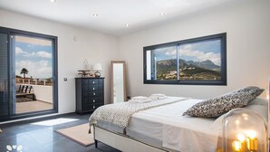 Un dormitorio moderno con una cama grande, un aparador, un espejo y vistas a las montañas a través de una ventana.