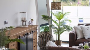 Una sala de estar moderna con un mueble de madera, un espejo grande, una lámpara colgante y una planta en maceta.